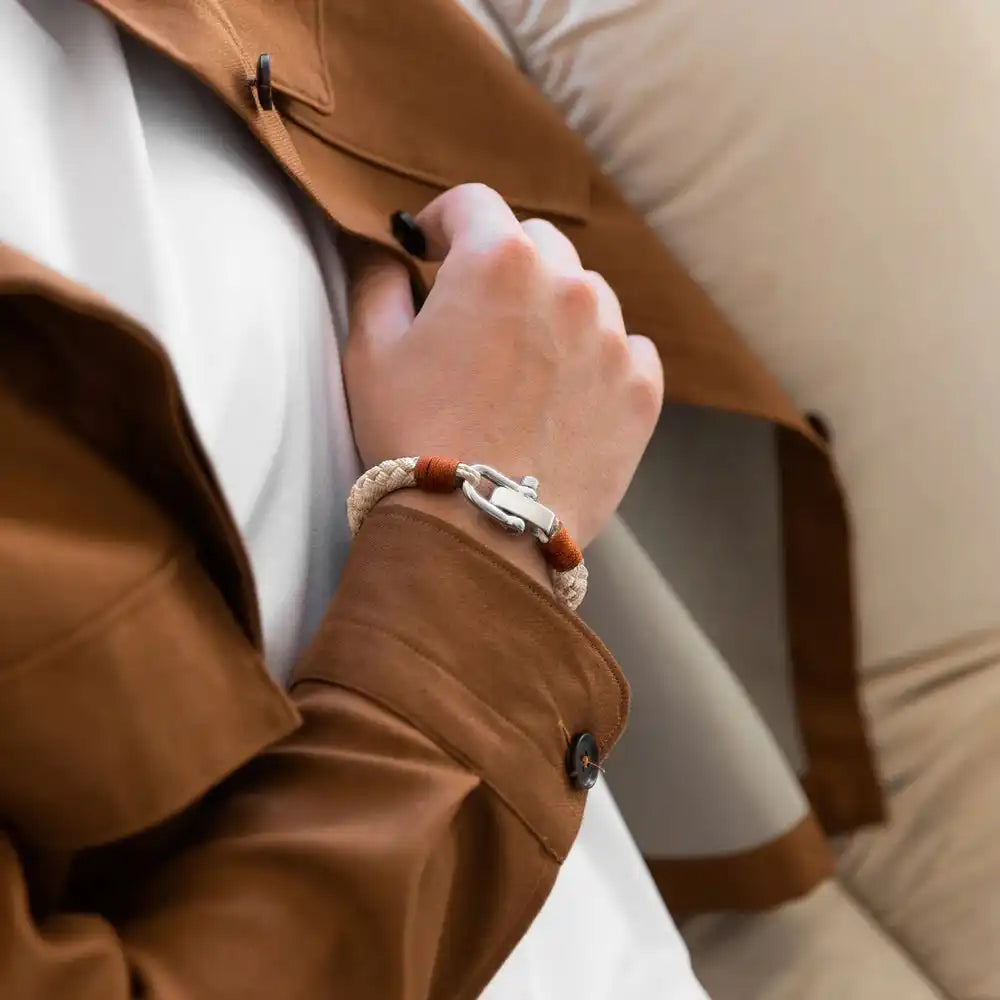 Le poignet d'une personne orné d'un bracelet tressé avec un fermoir à chaîne de couleur argentée.