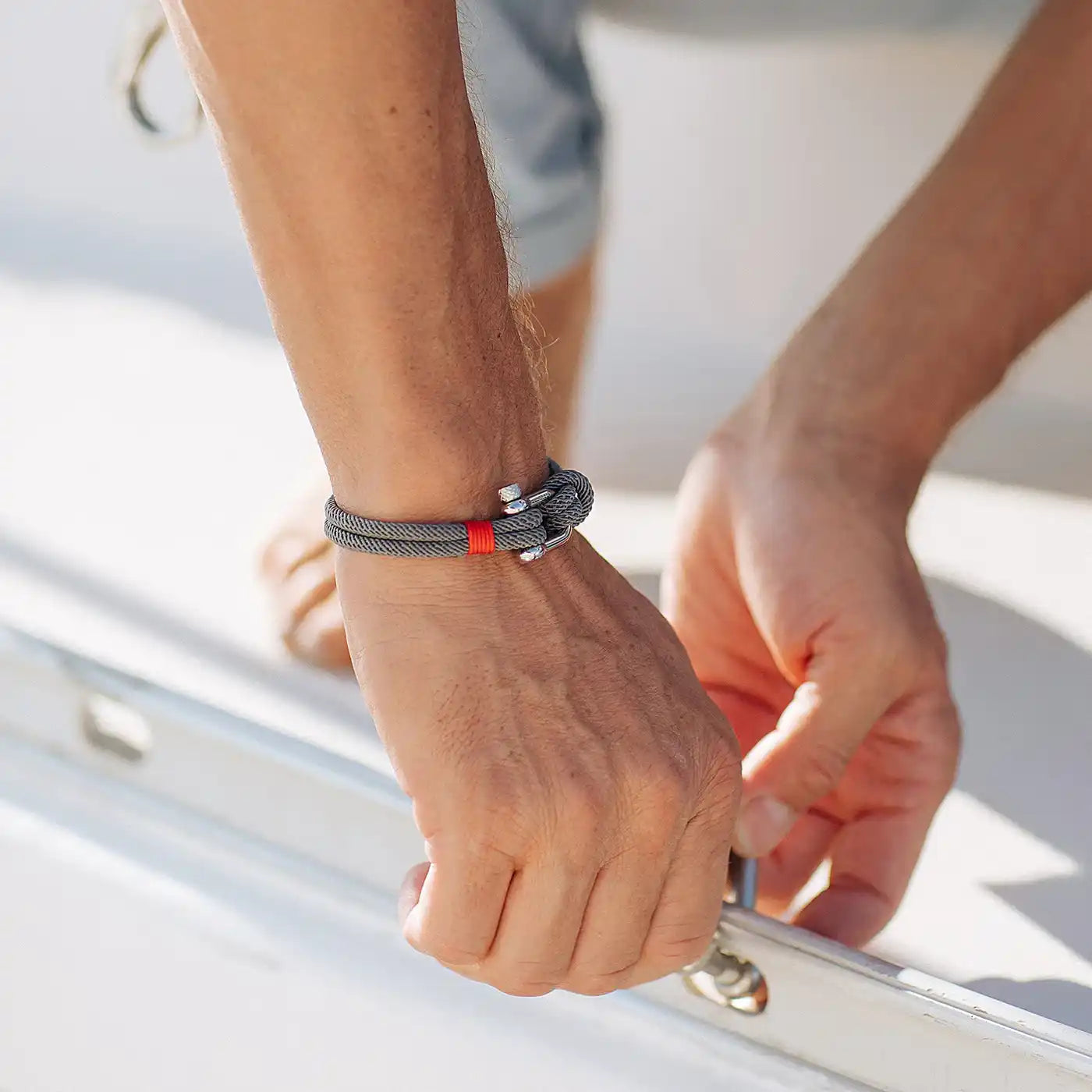 Un bracelet en corde grise avec une boucle en métal et une petite touche rouge.